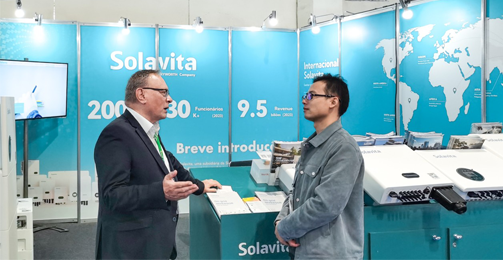 Solavita overseas sales team communicating with customer at Brazil solar exhibition booth, showcasing inverters and global business presence